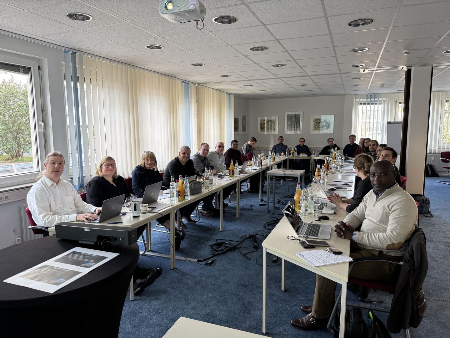Gruppenbesprechung mit Teilnehmern an Tischen und Laptops.